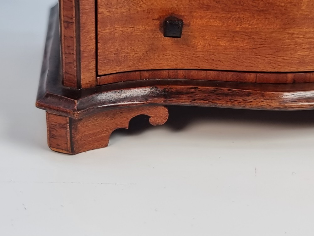 An Edwardian miniature satinwood chest of drawers featuring a serpentine front, inlaid shell medallion on the top, and four small drawers with wooden knobs. View XI