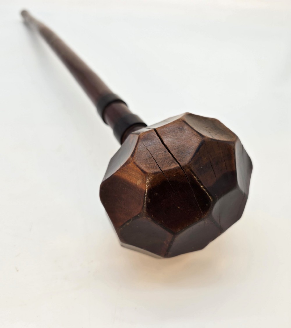 An antique dark hardwood Zulu knobkerrie club featuring a faceted spherical head and a slender shaft with raised carved rings near the top. View III