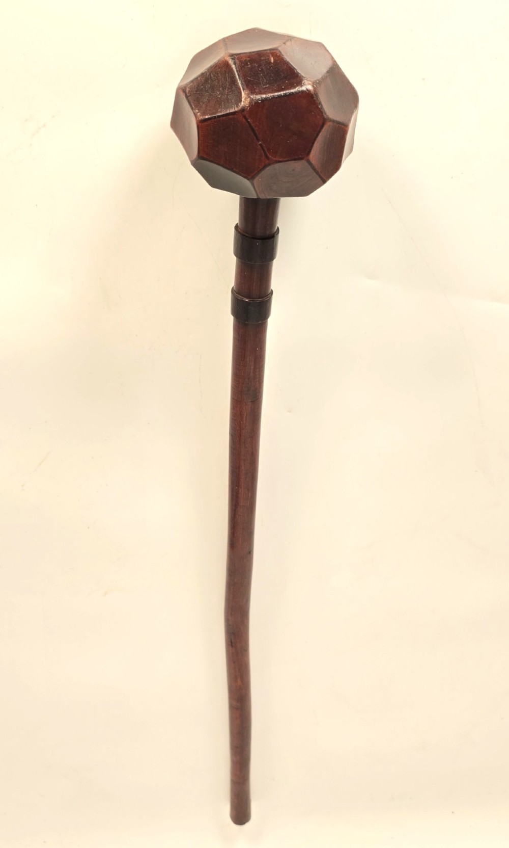 An antique dark hardwood Zulu knobkerrie club featuring a faceted spherical head and a slender shaft with raised carved rings near the top. View VIII