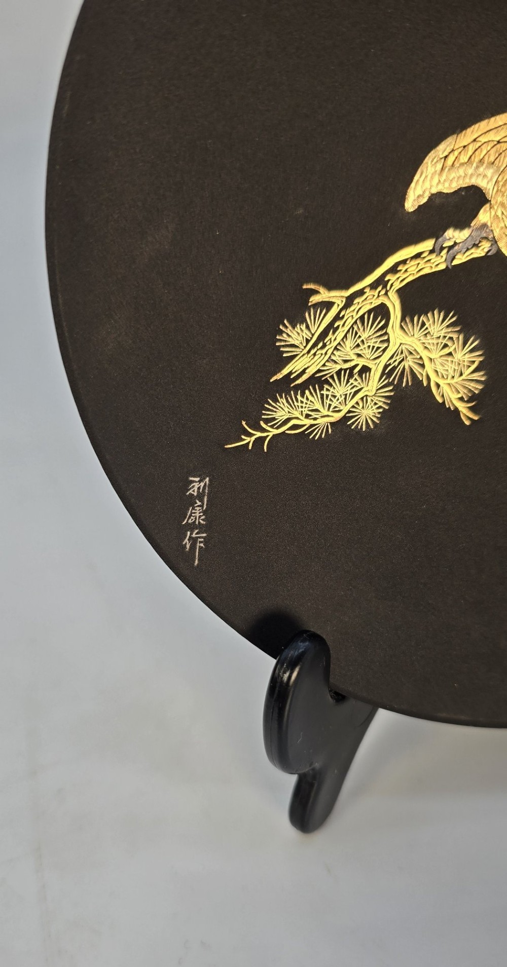 A circular black patinated iron plaque featuring an inlaid gold and silver depiction of an eagle perched on a pine branch. View V