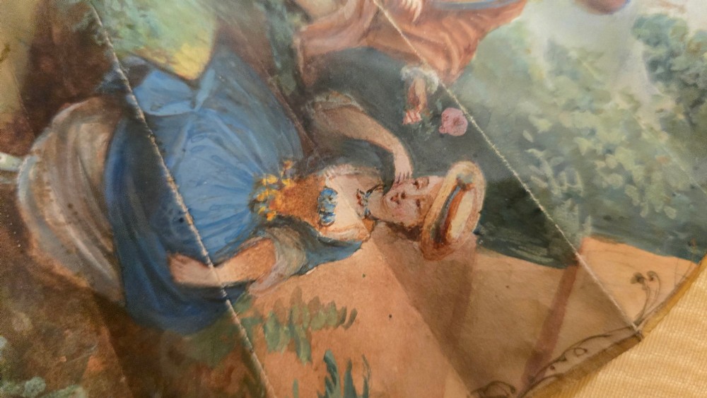A late 18th-century Italian folding fan featuring a hand-painted pastoral scene mounted on carved mother-of-pearl sticks, presented inside a fan-shaped black frame with a cream silk lining. View V