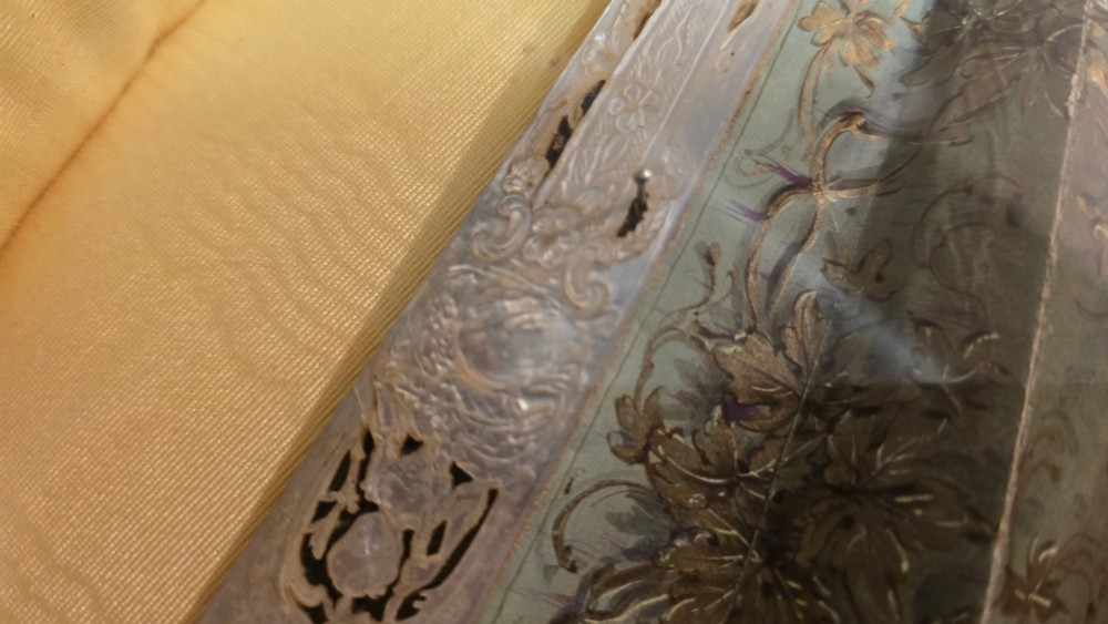 A late 18th-century Italian folding fan featuring a hand-painted pastoral scene mounted on carved mother-of-pearl sticks, presented inside a fan-shaped black frame with a cream silk lining. View VI
