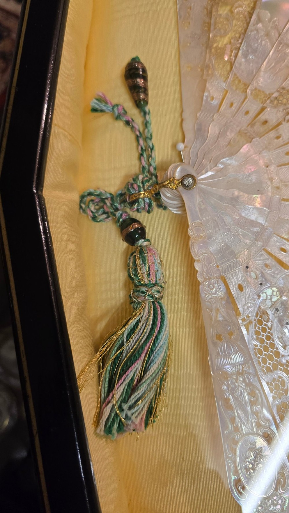 A late 18th-century Italian folding fan featuring a hand-painted pastoral scene mounted on carved mother-of-pearl sticks, presented inside a fan-shaped black frame with a cream silk lining. View VIII