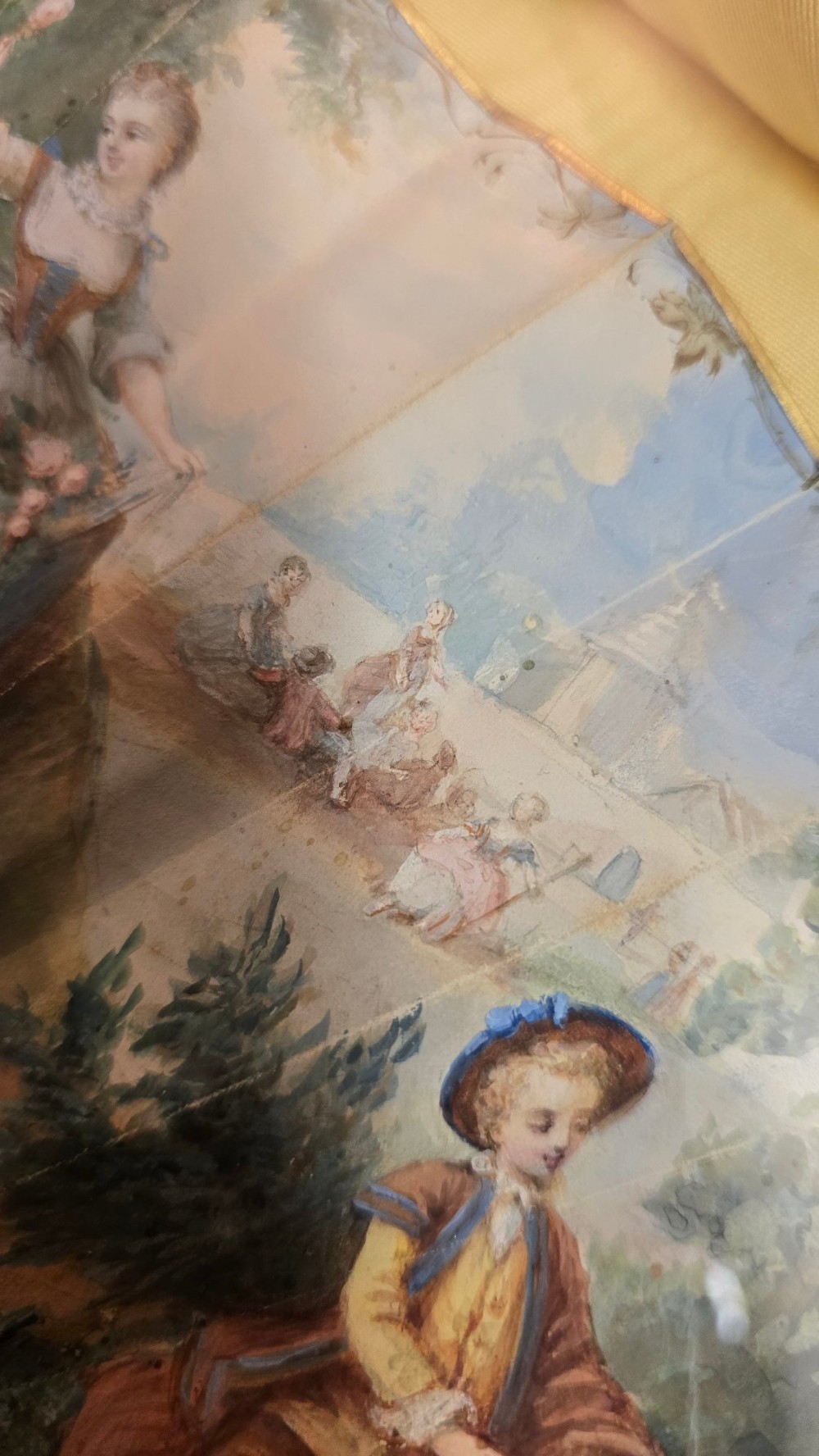 A late 18th-century Italian folding fan featuring a hand-painted pastoral scene mounted on carved mother-of-pearl sticks, presented inside a fan-shaped black frame with a cream silk lining. View X
