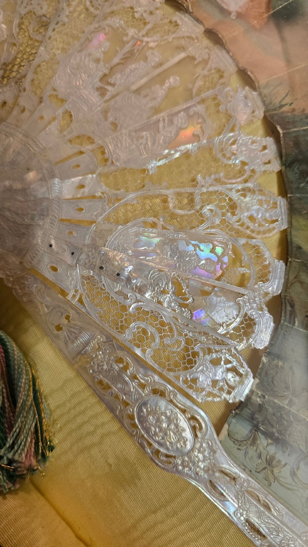 A late 18th-century Italian folding fan featuring a hand-painted pastoral scene mounted on carved mother-of-pearl sticks, presented inside a fan-shaped black frame with a cream silk lining. View XII