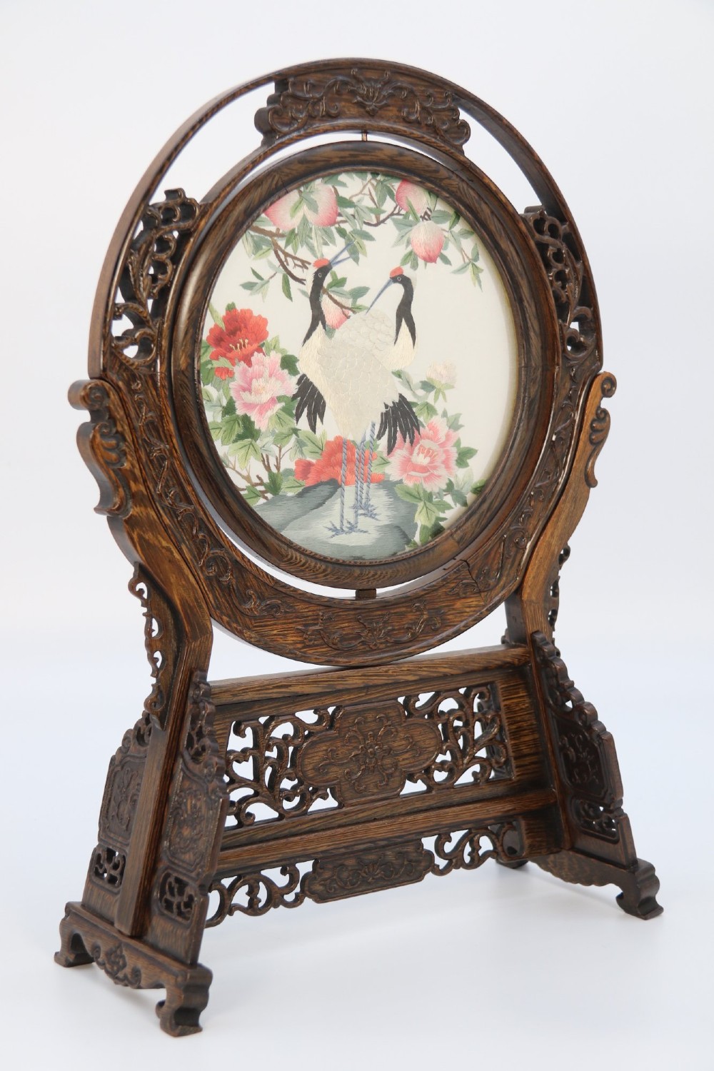 A circular double-sided silk embroidery depicting cranes among pink flowers, set within a rotating carved dark hardwood frame and stand.