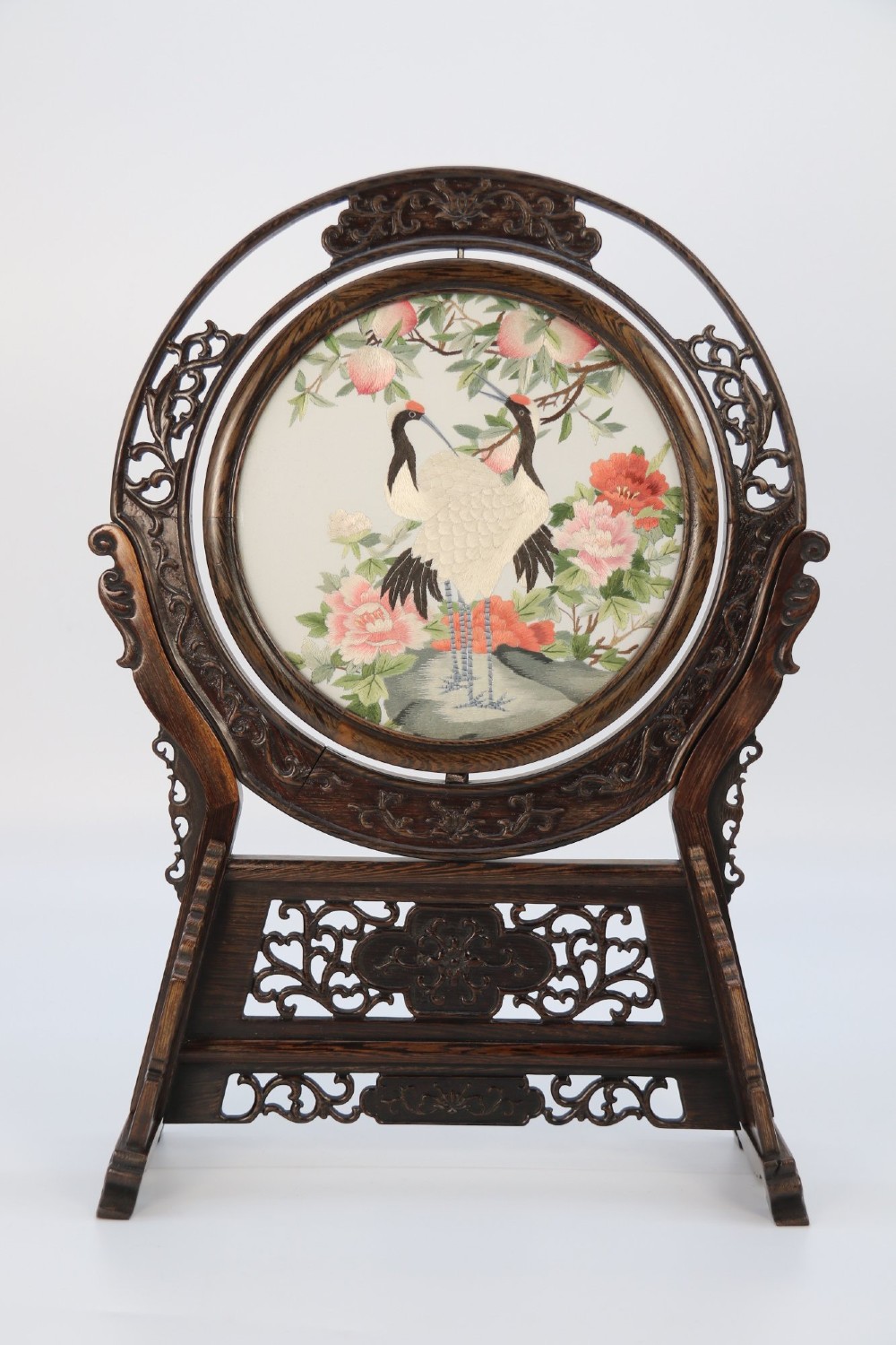A circular double-sided silk embroidery depicting cranes among pink flowers, set within a rotating carved dark hardwood frame and stand. View II