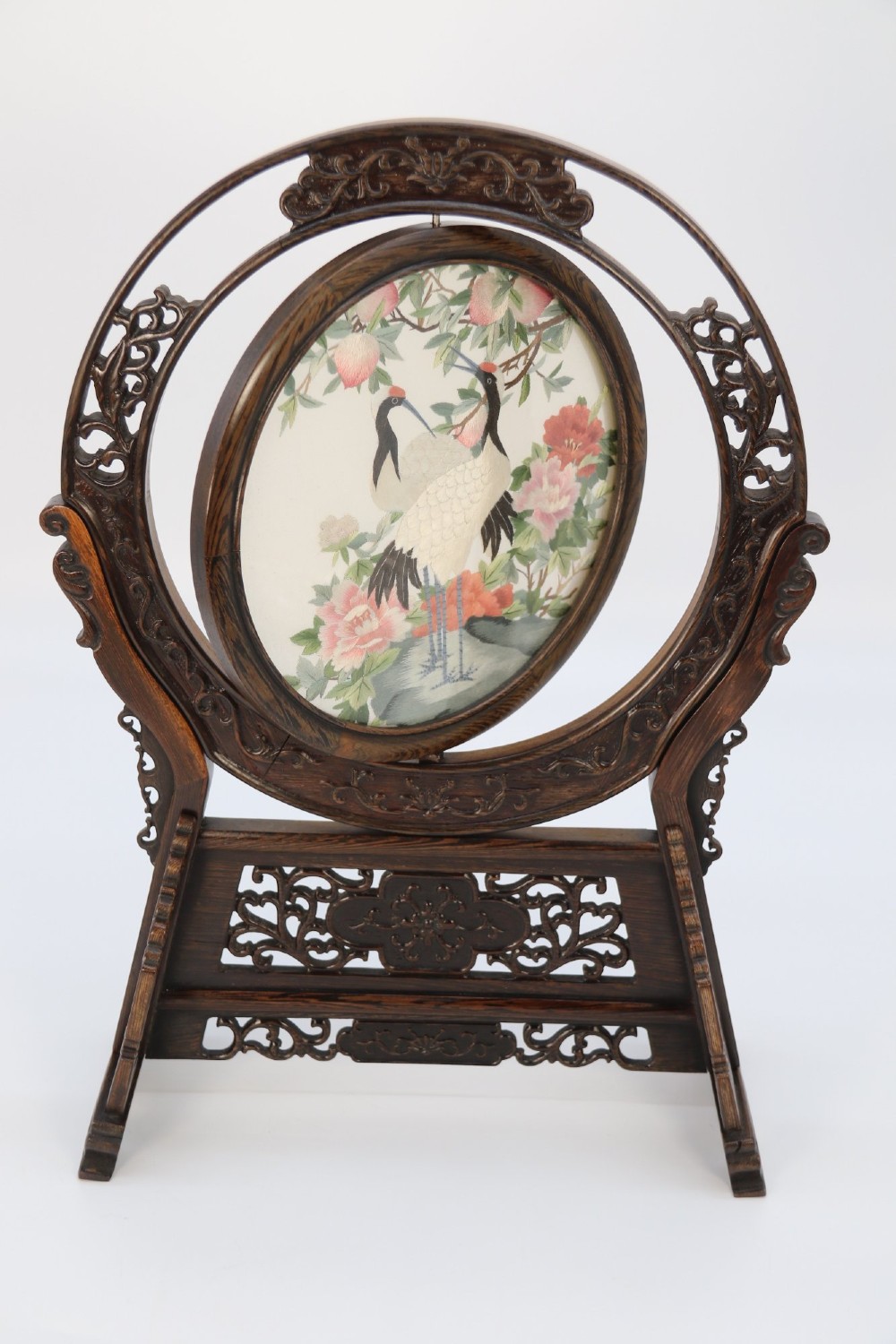 A circular double-sided silk embroidery depicting cranes among pink flowers, set within a rotating carved dark hardwood frame and stand. View IV