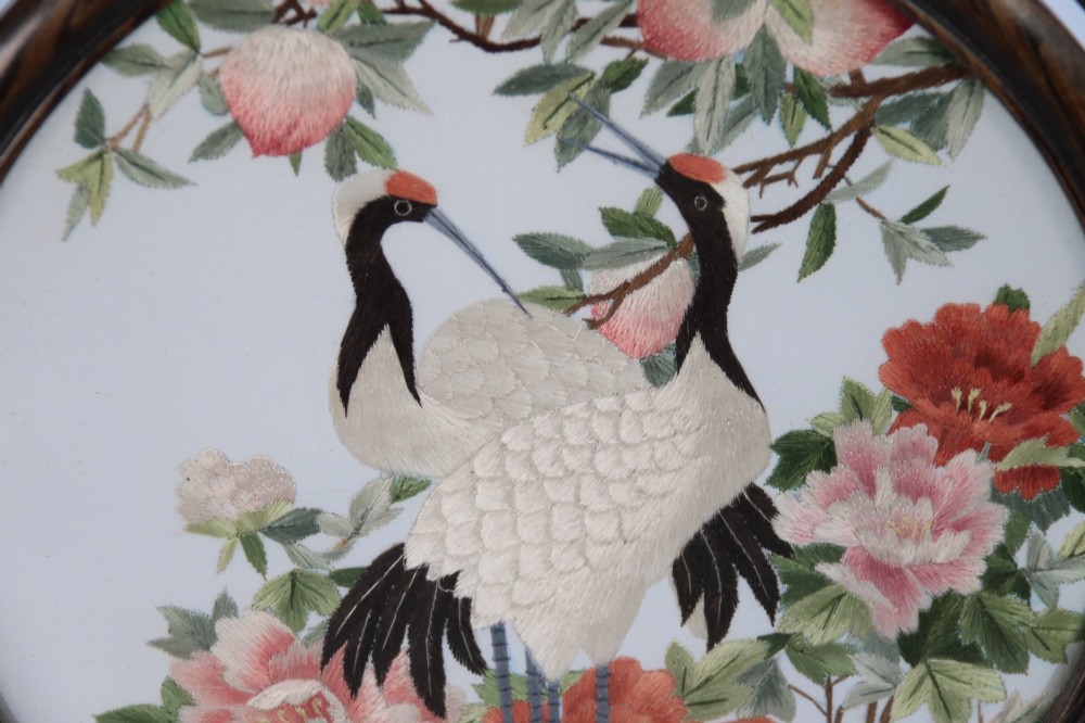 A circular double-sided silk embroidery depicting cranes among pink flowers, set within a rotating carved dark hardwood frame and stand. View VII