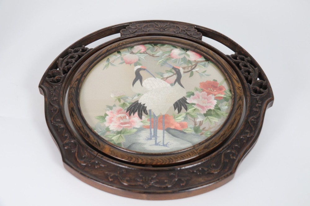 A circular double-sided silk embroidery depicting cranes among pink flowers, set within a rotating carved dark hardwood frame and stand. View XI