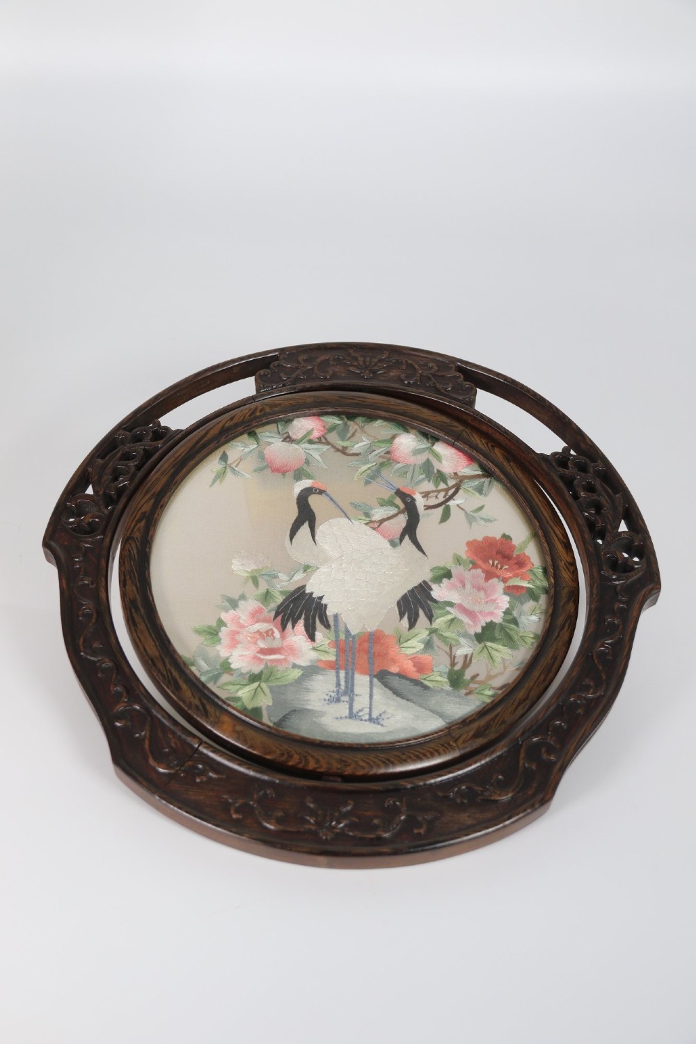 A circular double-sided silk embroidery depicting cranes among pink flowers, set within a rotating carved dark hardwood frame and stand. View XII