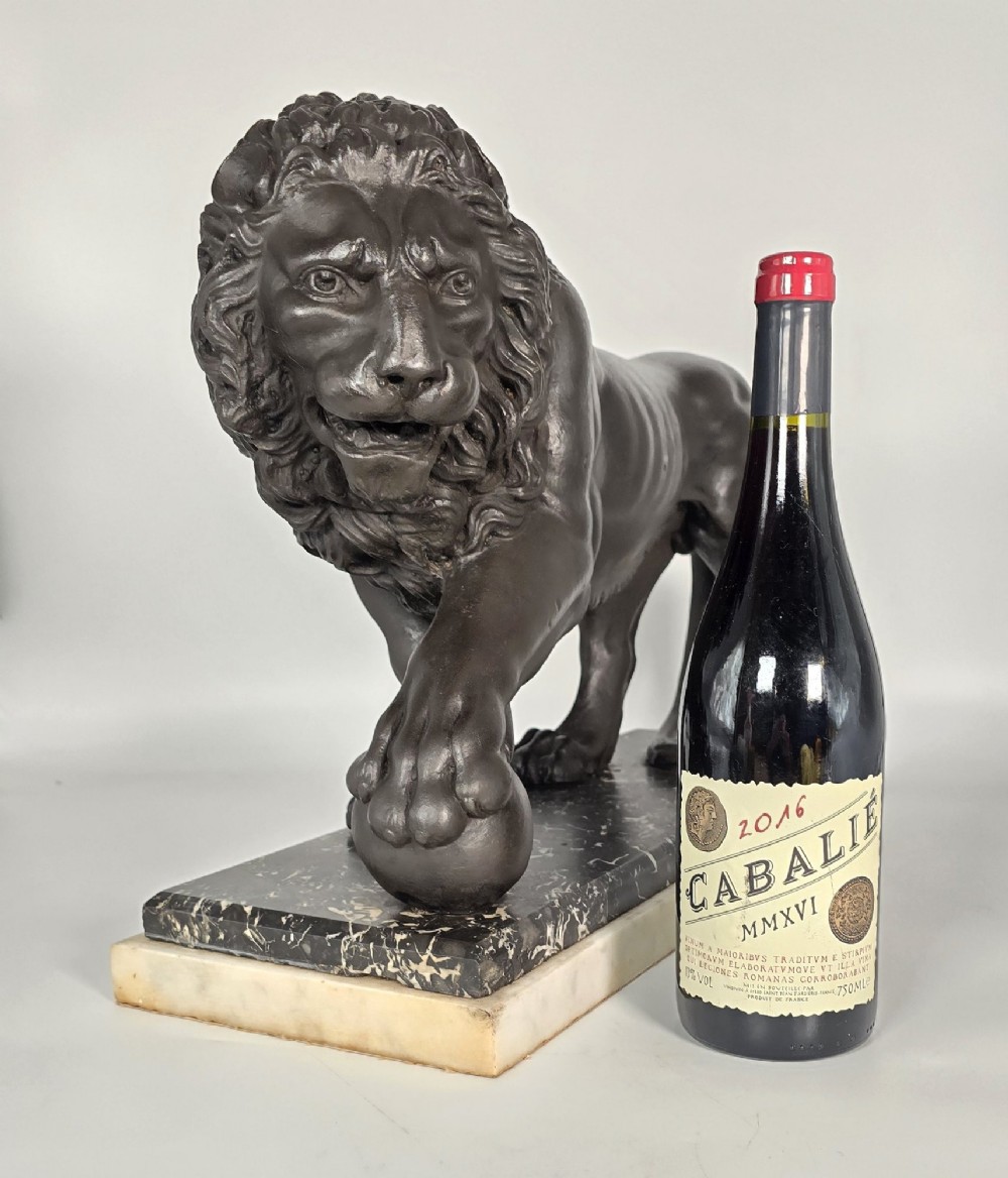 A dark patinated bronze sculpture of a lion resting its paw on a sphere, mounted on a two-tier marble plinth. View II