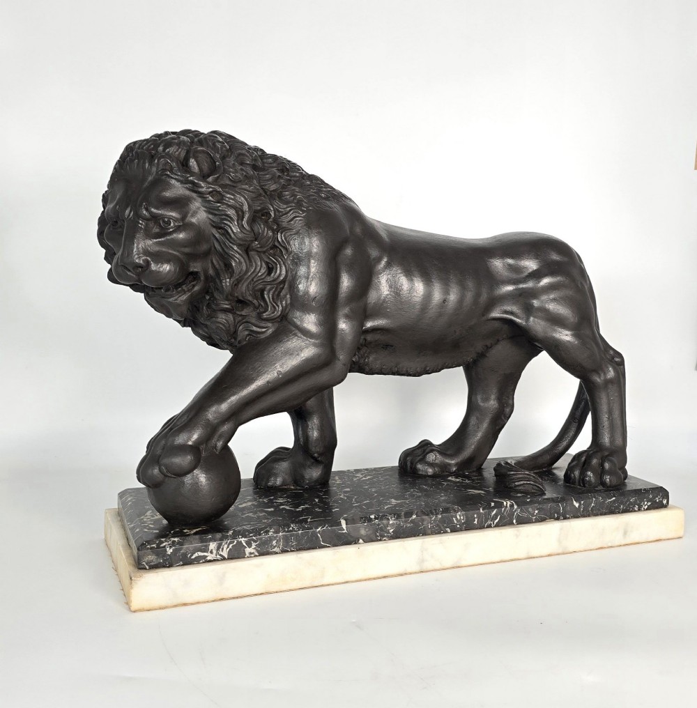 A dark patinated bronze sculpture of a lion resting its paw on a sphere, mounted on a two-tier marble plinth. View III