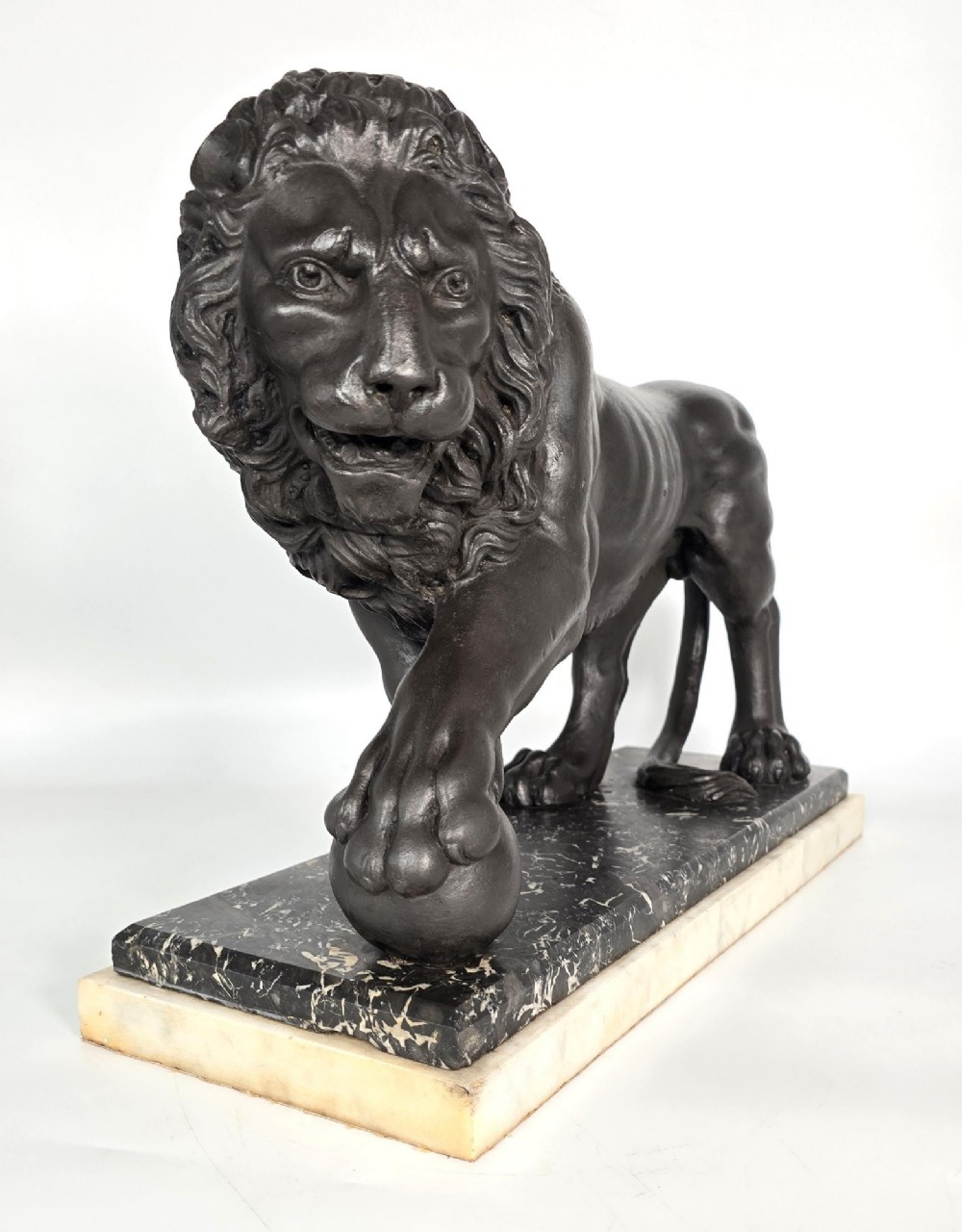A dark patinated bronze sculpture of a lion resting its paw on a sphere, mounted on a two-tier marble plinth. View IV