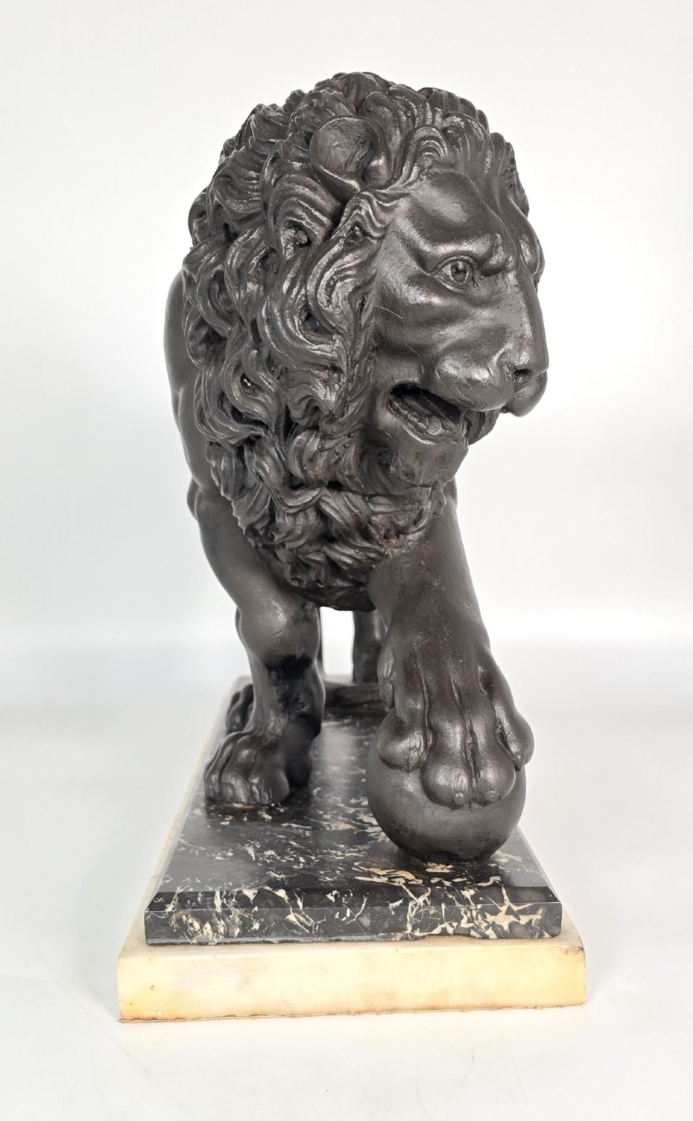 A dark patinated bronze sculpture of a lion resting its paw on a sphere, mounted on a two-tier marble plinth. View V