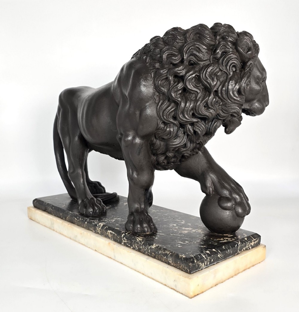 A dark patinated bronze sculpture of a lion resting its paw on a sphere, mounted on a two-tier marble plinth. View VI