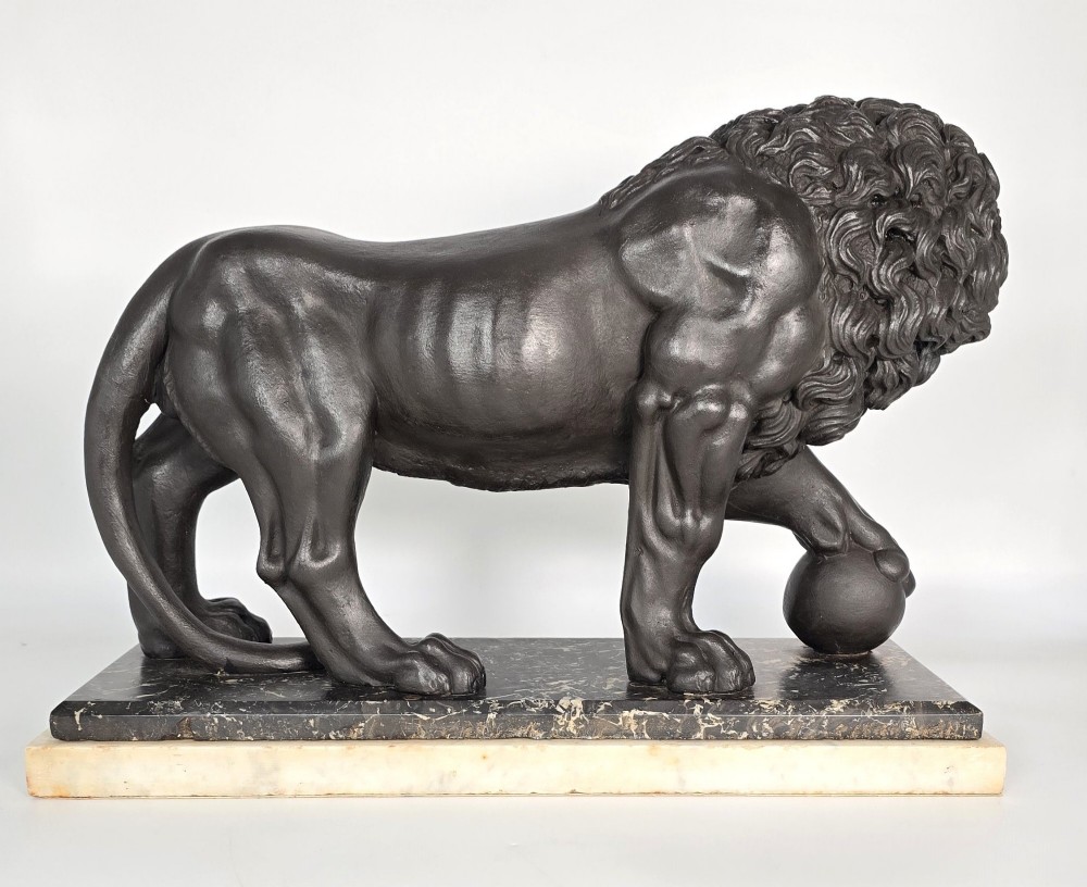 A dark patinated bronze sculpture of a lion resting its paw on a sphere, mounted on a two-tier marble plinth. View VII
