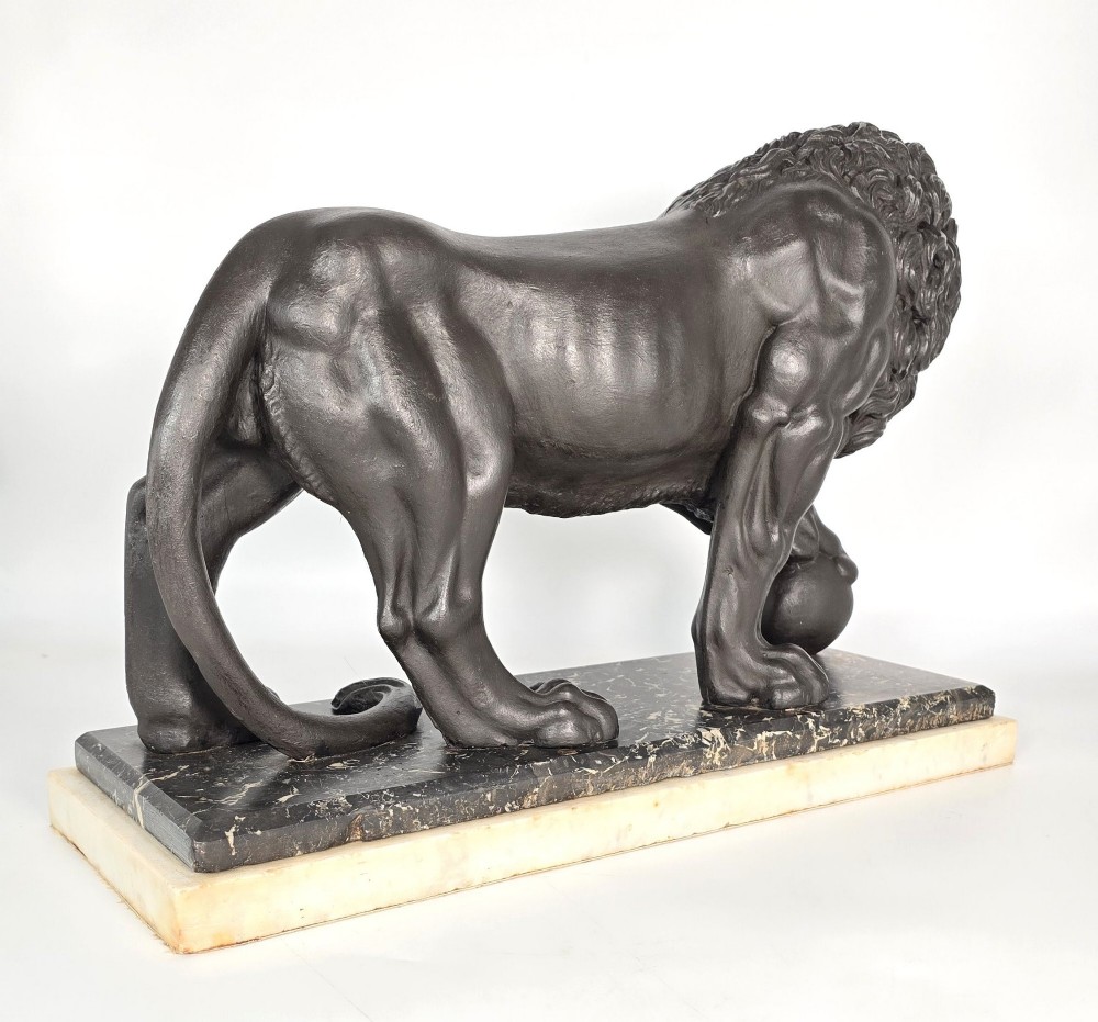 A dark patinated bronze sculpture of a lion resting its paw on a sphere, mounted on a two-tier marble plinth. View VIII