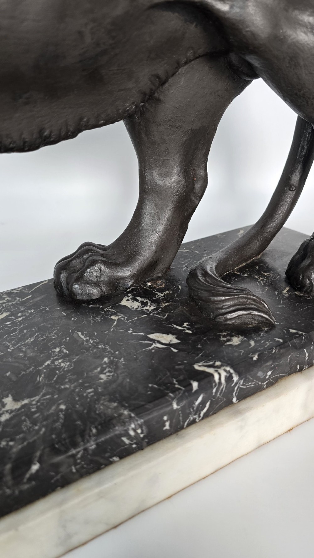 A dark patinated bronze sculpture of a lion resting its paw on a sphere, mounted on a two-tier marble plinth. View X