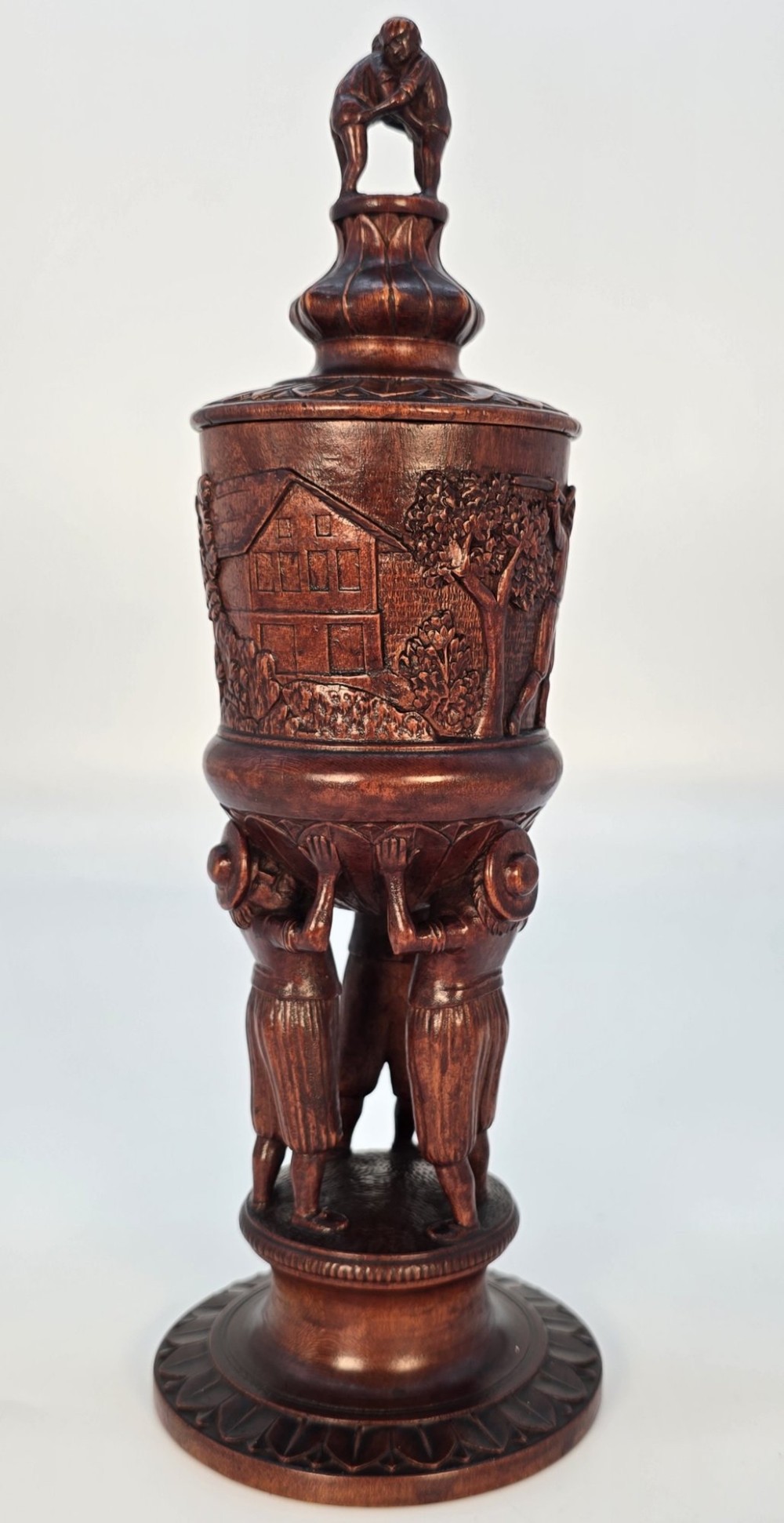 A tall hand-carved dark walnut lidded chalice featuring a stem sculpted as human figures, a relief carving of cattle around the vessel, and a finial with carved figures. View II