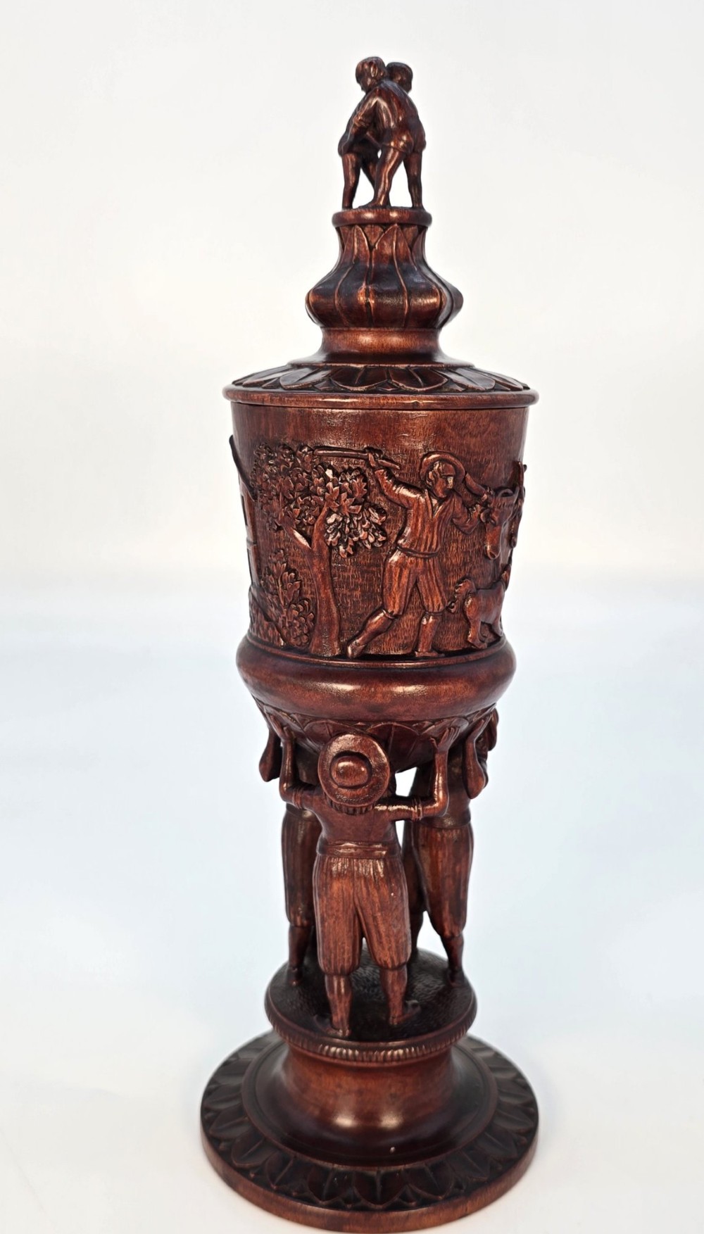A tall hand-carved dark walnut lidded chalice featuring a stem sculpted as human figures, a relief carving of cattle around the vessel, and a finial with carved figures. View IV