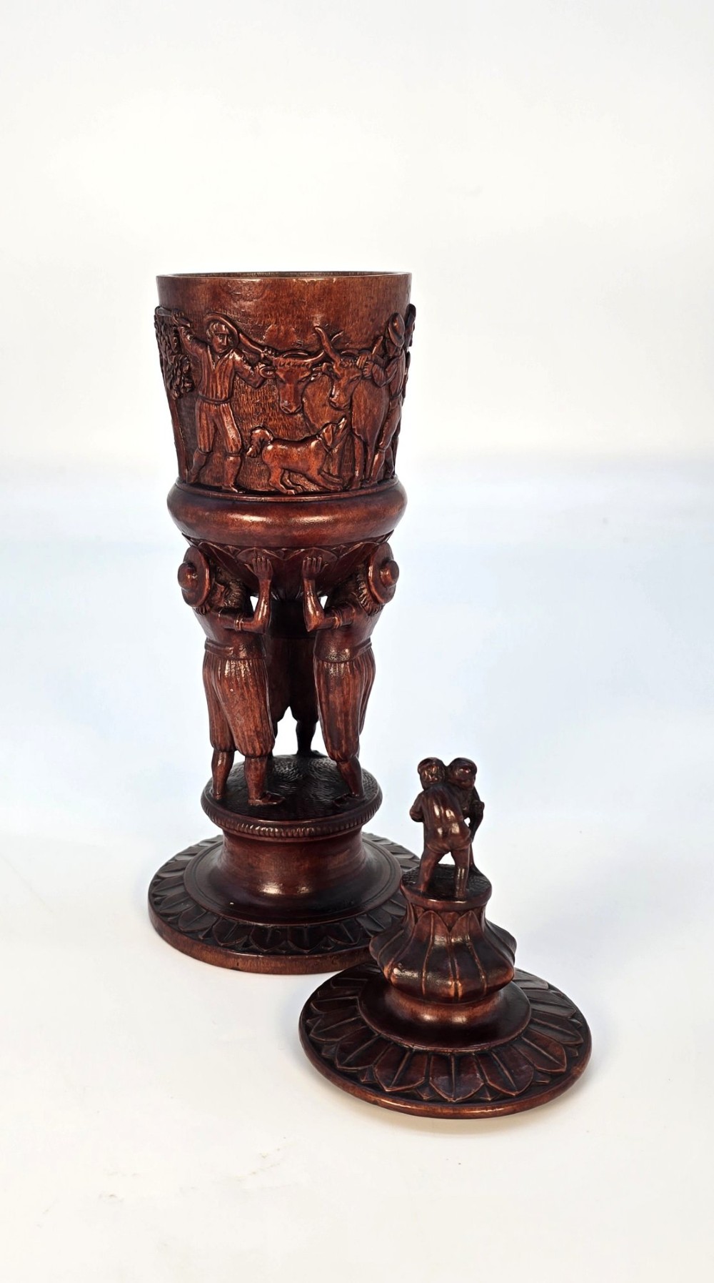 A tall hand-carved dark walnut lidded chalice featuring a stem sculpted as human figures, a relief carving of cattle around the vessel, and a finial with carved figures. View VI