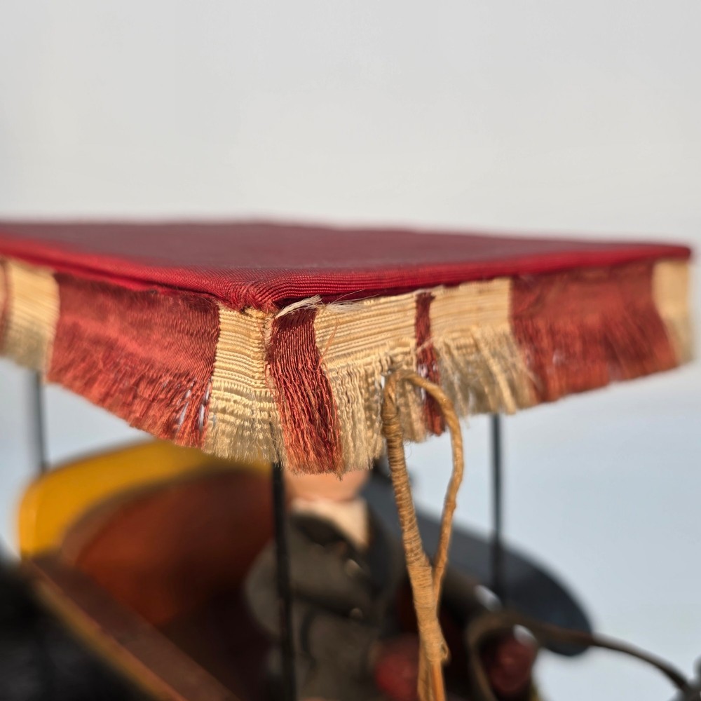 A hand-crafted 1928 wooden folk art model featuring a brown horse attached to a yellow two-wheeled chaise carriage with a driver figure under a striped canopy, mounted on a dark wooden base. View VII
