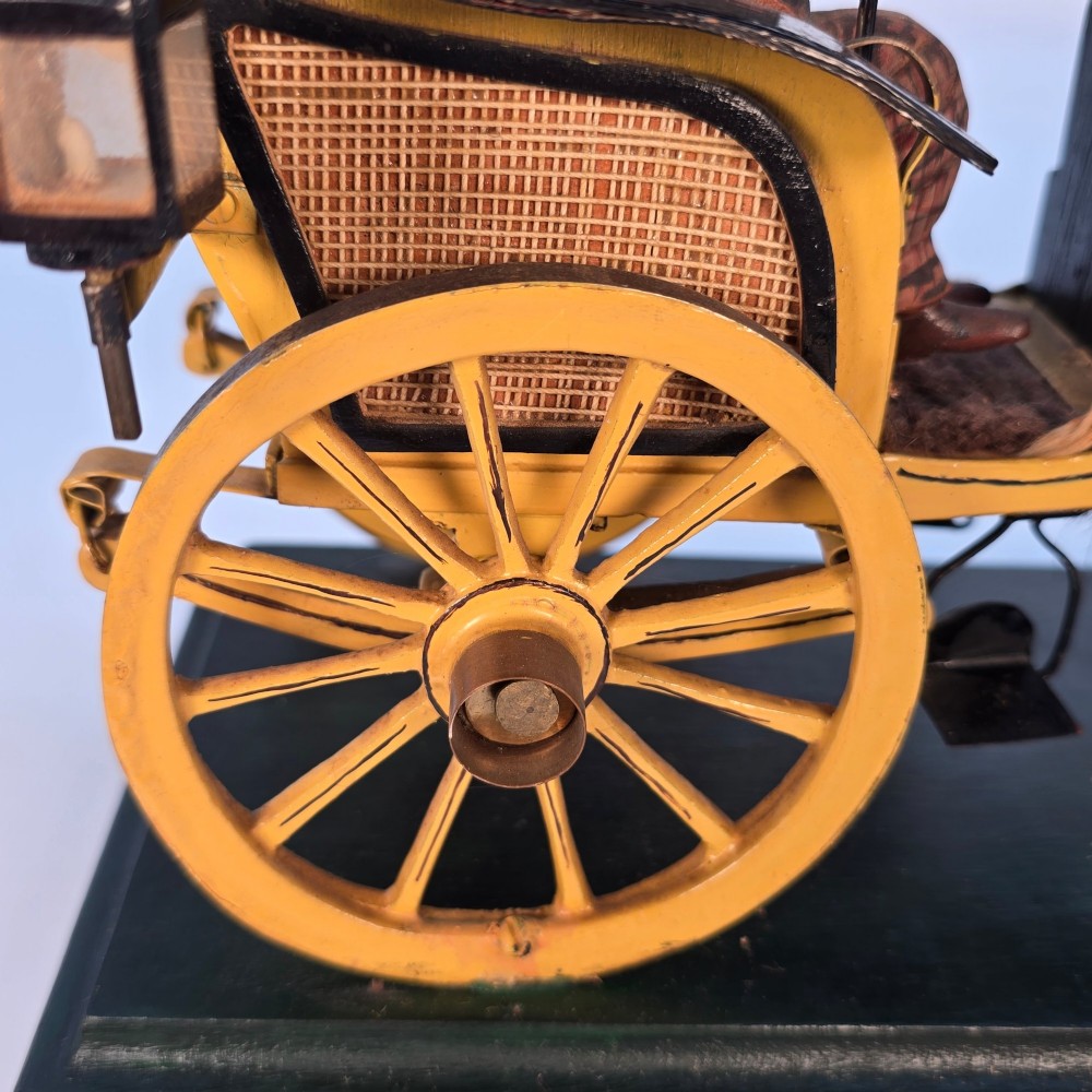 A hand-crafted 1928 wooden folk art model featuring a brown horse attached to a yellow two-wheeled chaise carriage with a driver figure under a striped canopy, mounted on a dark wooden base. View VIII