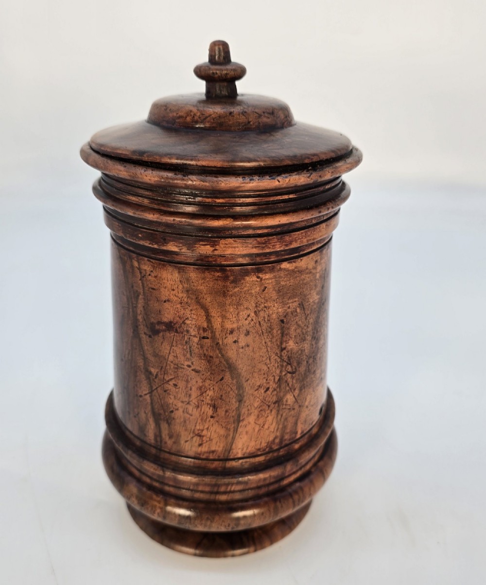 An 18th-century turned walnut wooden tobacco jar featuring a knopped finial lid, turned mouldings, and a dark aged grain surface.