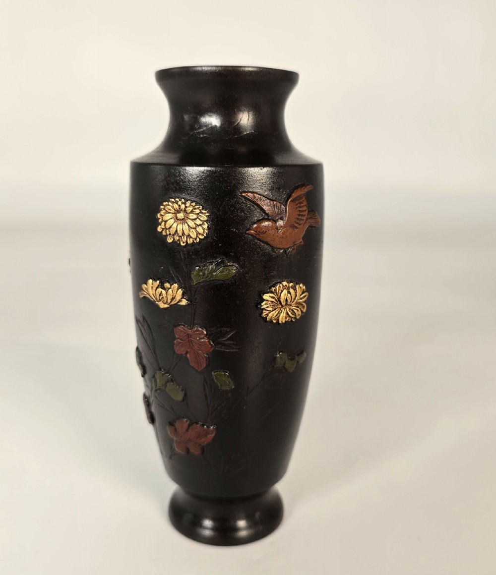 A dark brown patinated bronze Japanese vase featuring raised relief inlays of gold and copper chrysanthemums alongside a bird in flight.