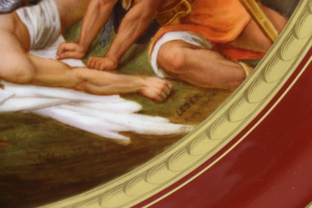 A large round porcelain charger with a deep burgundy border edged in gold leaf, featuring a central hand-painted scene depicting a historic battle with figures on horseback. View III