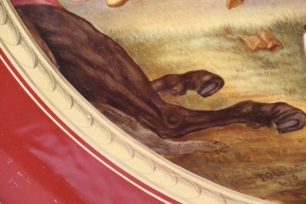 A large round porcelain charger with a deep burgundy border edged in gold leaf, featuring a central hand-painted scene depicting a historic battle with figures on horseback. View X