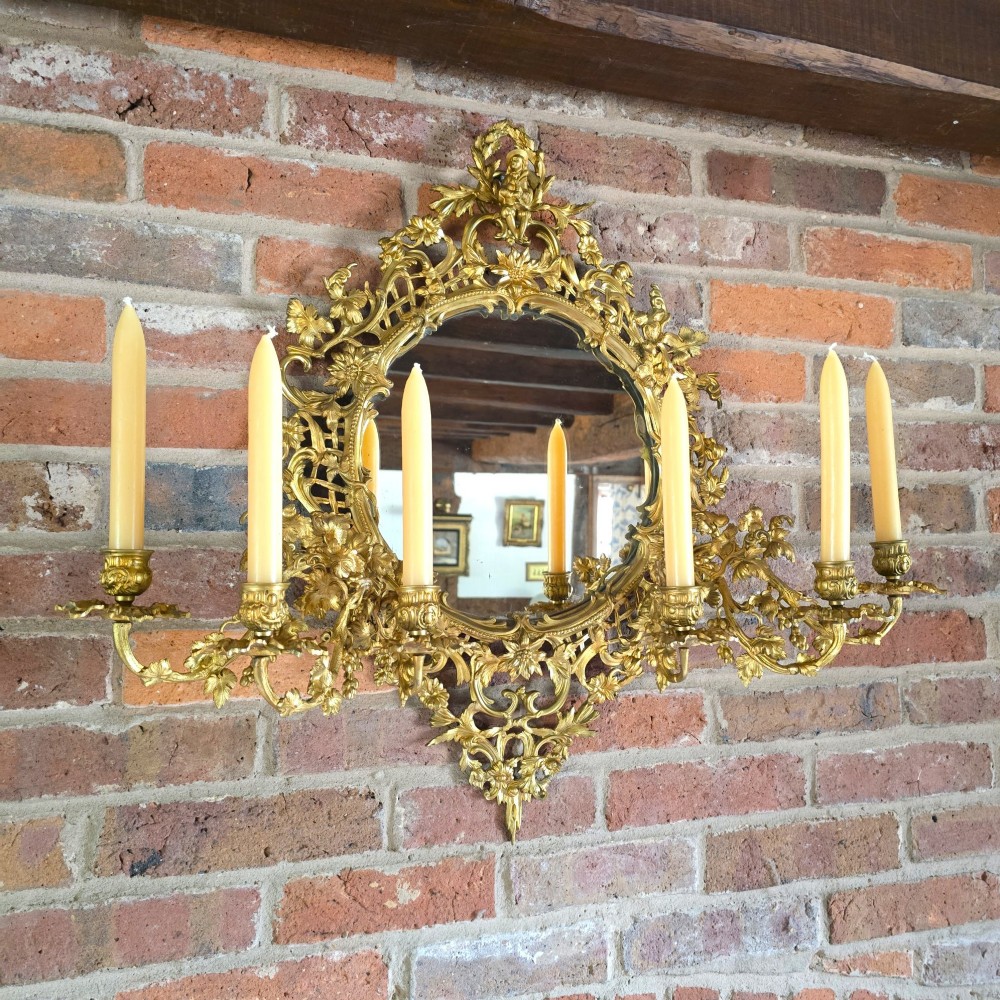 A 19th-century French ormolu girandole wall mirror featuring an ornate foliage frame, central oval mirror, and six branching candle arms.