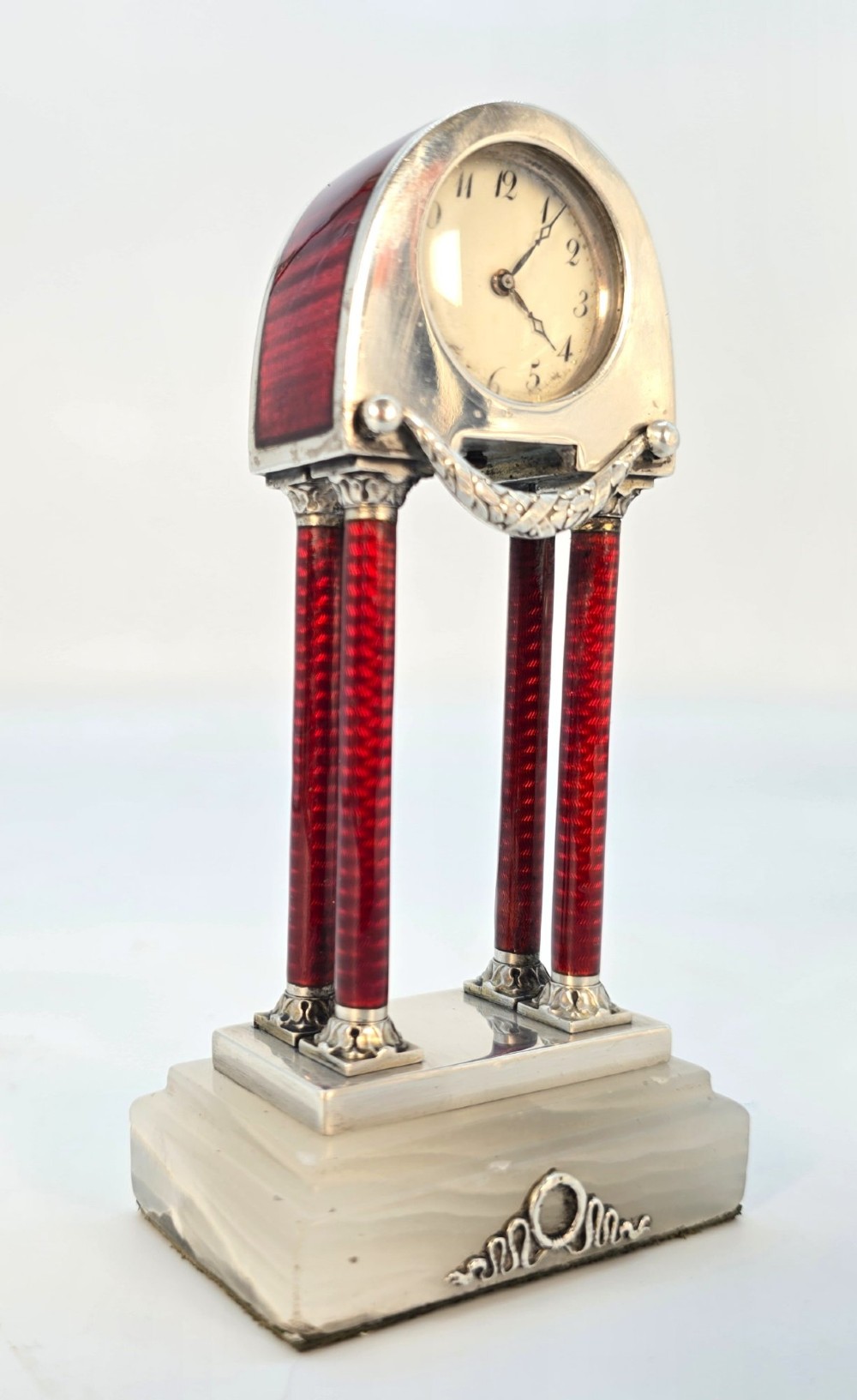 A Viennese silver and red guilloche enamel miniature portico desk clock mounted on a white onyx base.