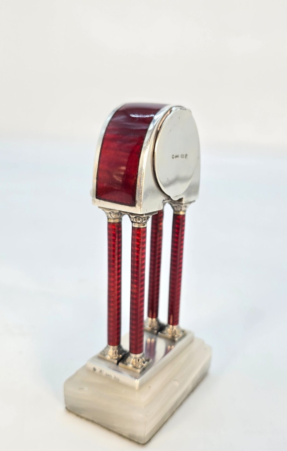 A Viennese silver and red guilloche enamel miniature portico desk clock mounted on a white onyx base. View V