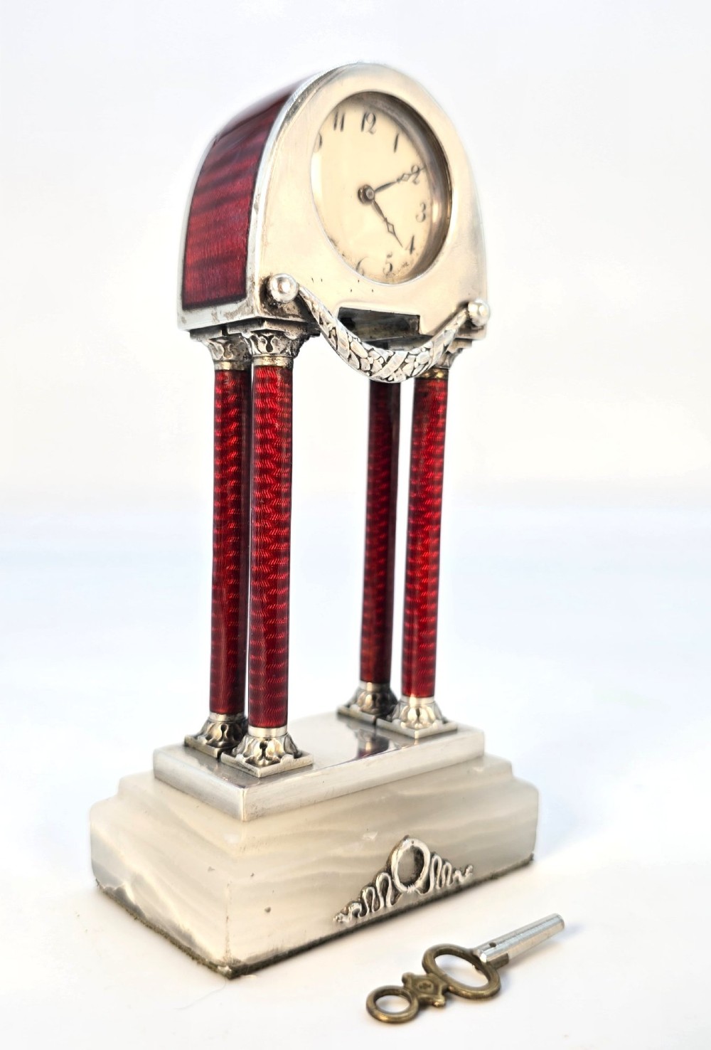 A Viennese silver and red guilloche enamel miniature portico desk clock mounted on a white onyx base. View XII