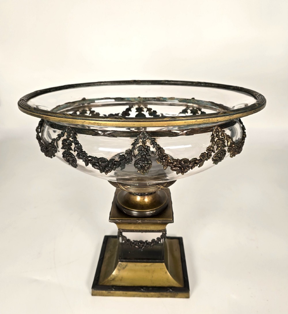A clear glass bowl mounted with gilt-bronze floral swags and supported by a square stepped pedestal base.
