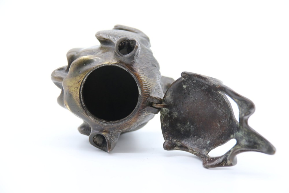 A dark cast bronze novelty inkwell sculpted in the form of a grotesque grinning face with textured hair and small footed base. View VI