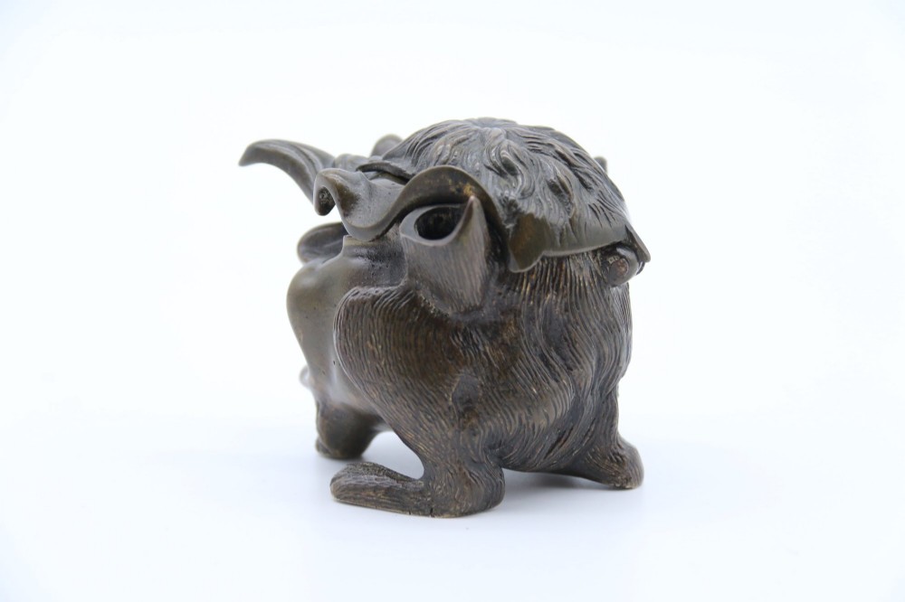 A dark cast bronze novelty inkwell sculpted in the form of a grotesque grinning face with textured hair and small footed base. View XV