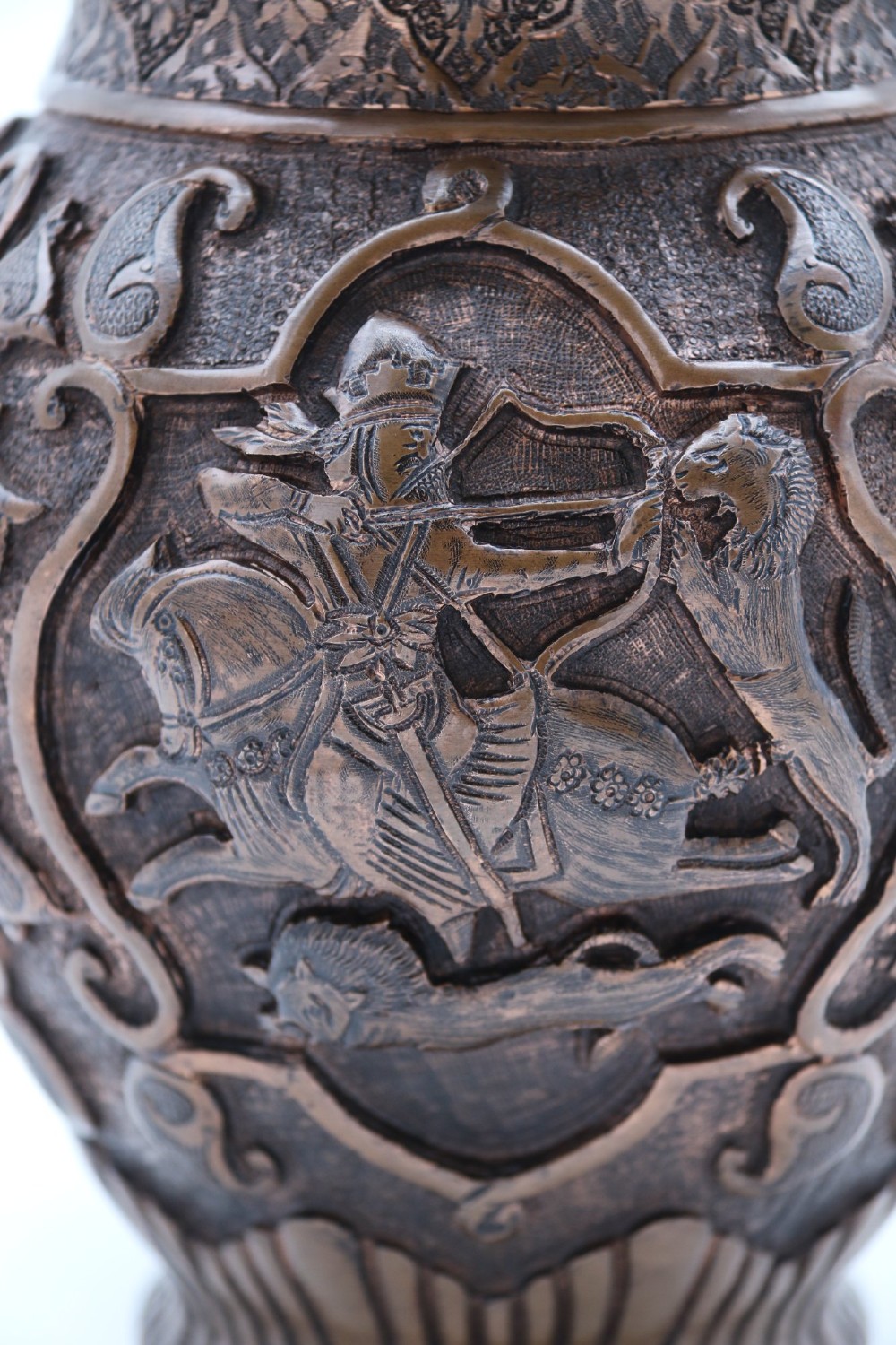 A bulbous late nineteenth-century copper vase featuring detailed repousse carvings of a mounted archer within a central cartouche surrounded by scrollwork and a fluted base. View XII