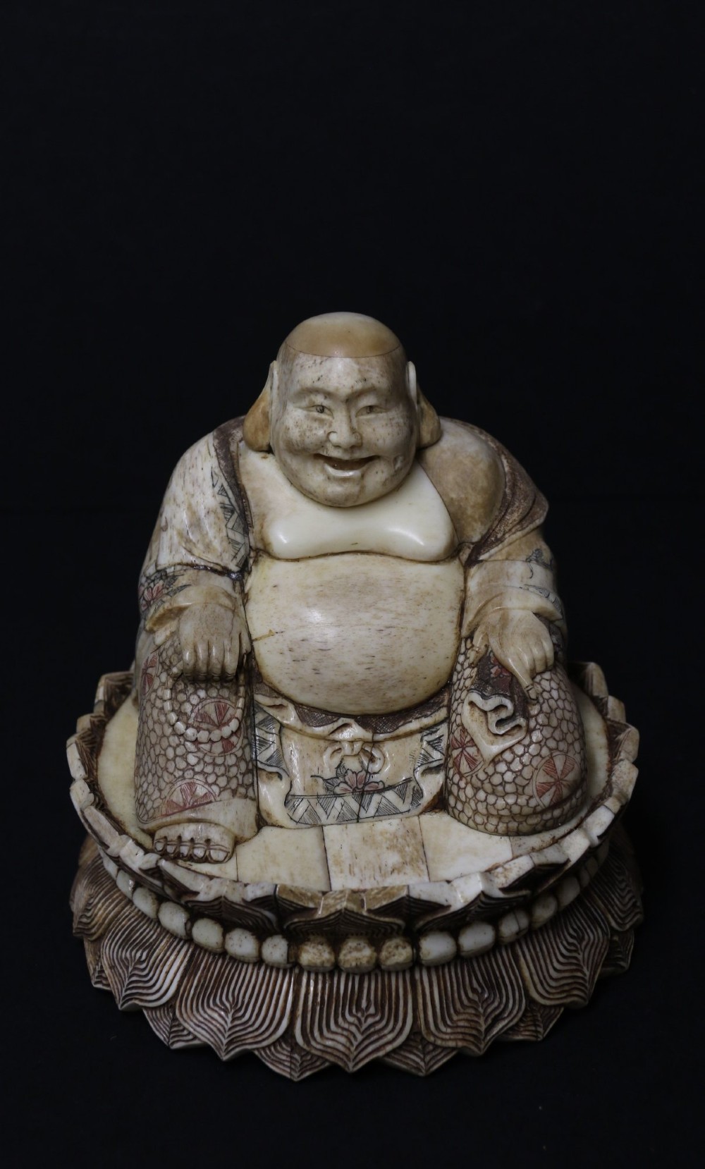 A Japanese carved bone okimono depicting a seated Buddha figure on an engraved lotus base with intricate ink detailing.