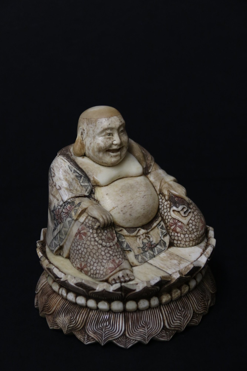 A Japanese carved bone okimono depicting a seated Buddha figure on an engraved lotus base with intricate ink detailing. View II