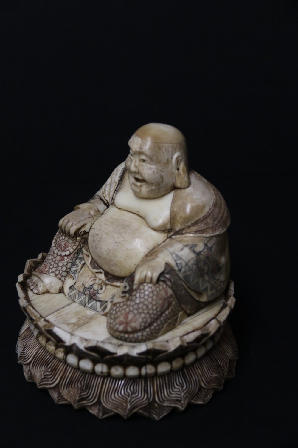 A Japanese carved bone okimono depicting a seated Buddha figure on an engraved lotus base with intricate ink detailing. View VII
