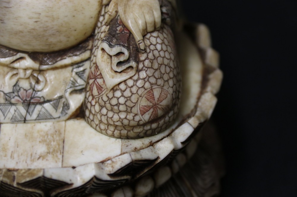A Japanese carved bone okimono depicting a seated Buddha figure on an engraved lotus base with intricate ink detailing. View VIII