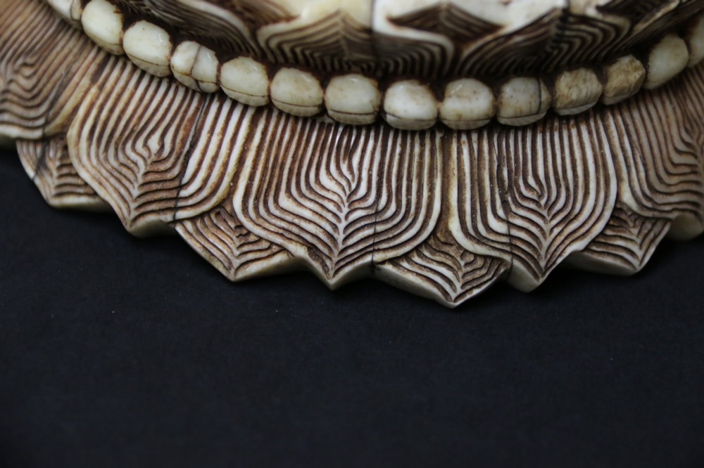 A Japanese carved bone okimono depicting a seated Buddha figure on an engraved lotus base with intricate ink detailing. View IX