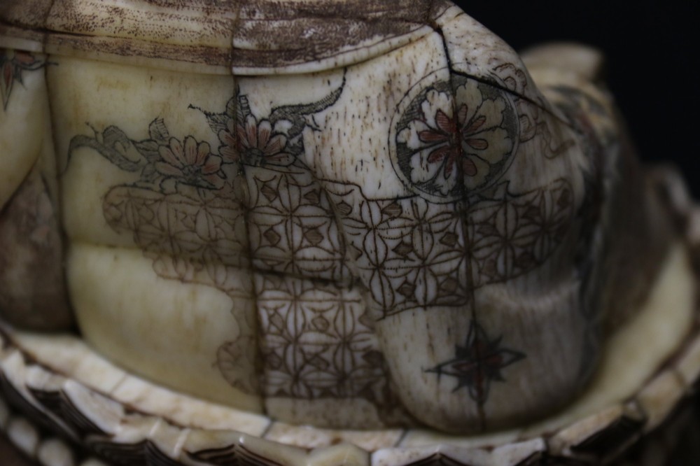 A Japanese carved bone okimono depicting a seated Buddha figure on an engraved lotus base with intricate ink detailing. View X
