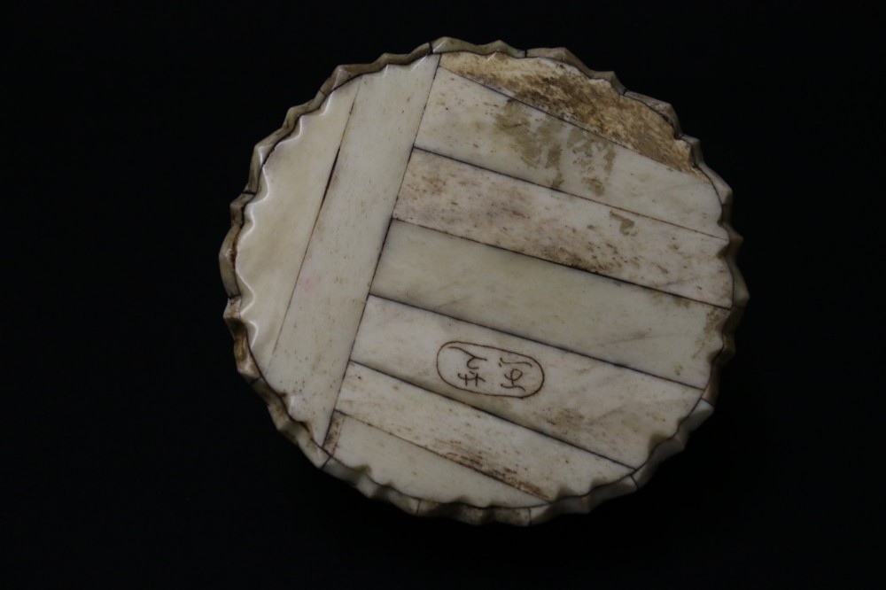 A Japanese carved bone okimono depicting a seated Buddha figure on an engraved lotus base with intricate ink detailing. View XI