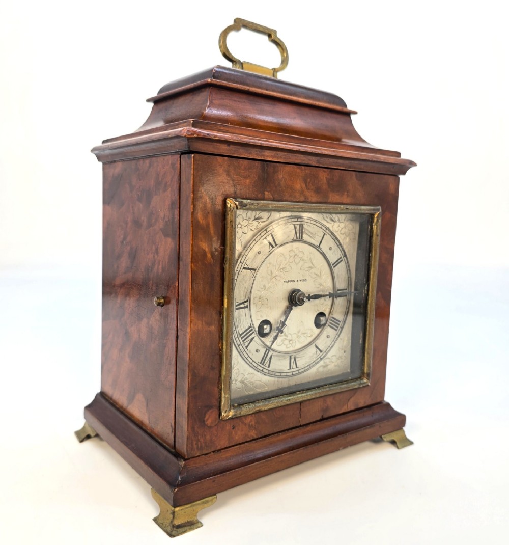 A miniature George II style wooden bracket clock featuring a caddy top with brass handle, engraved silvered dial with Roman numerals, and brass feet.