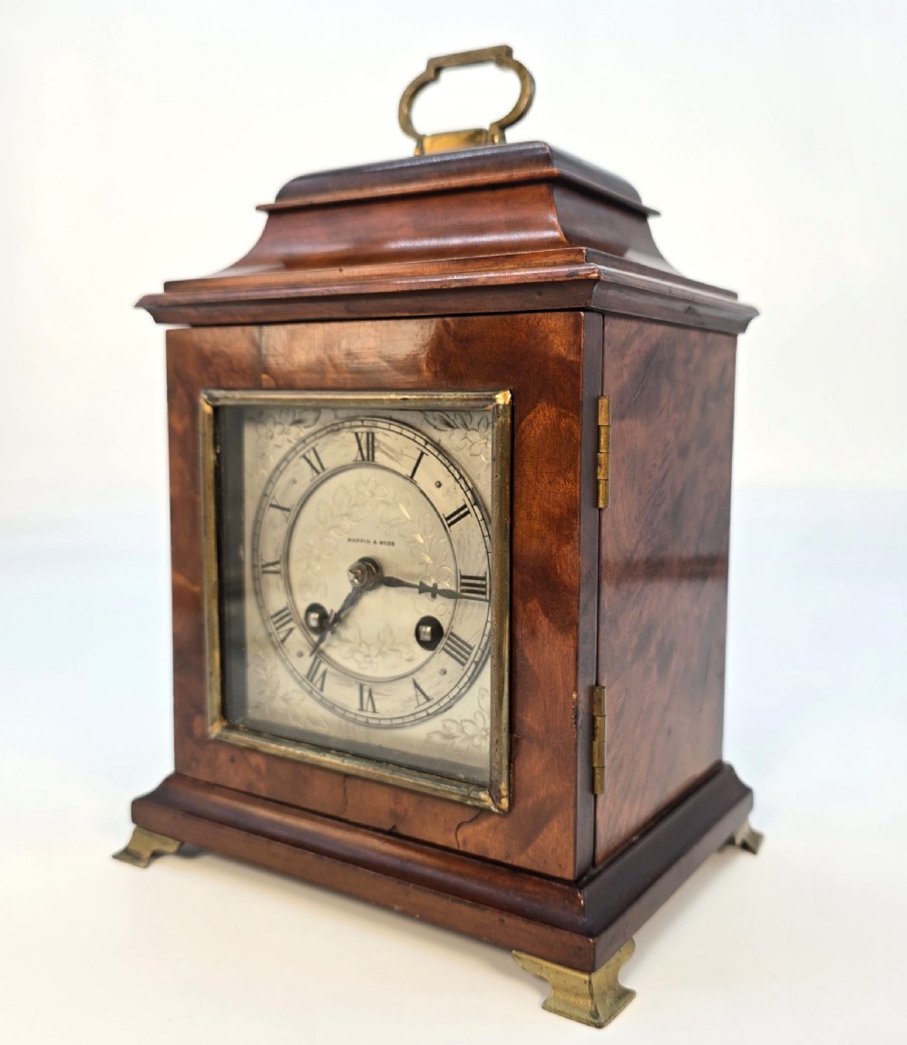 A miniature George II style wooden bracket clock featuring a caddy top with brass handle, engraved silvered dial with Roman numerals, and brass feet. View III