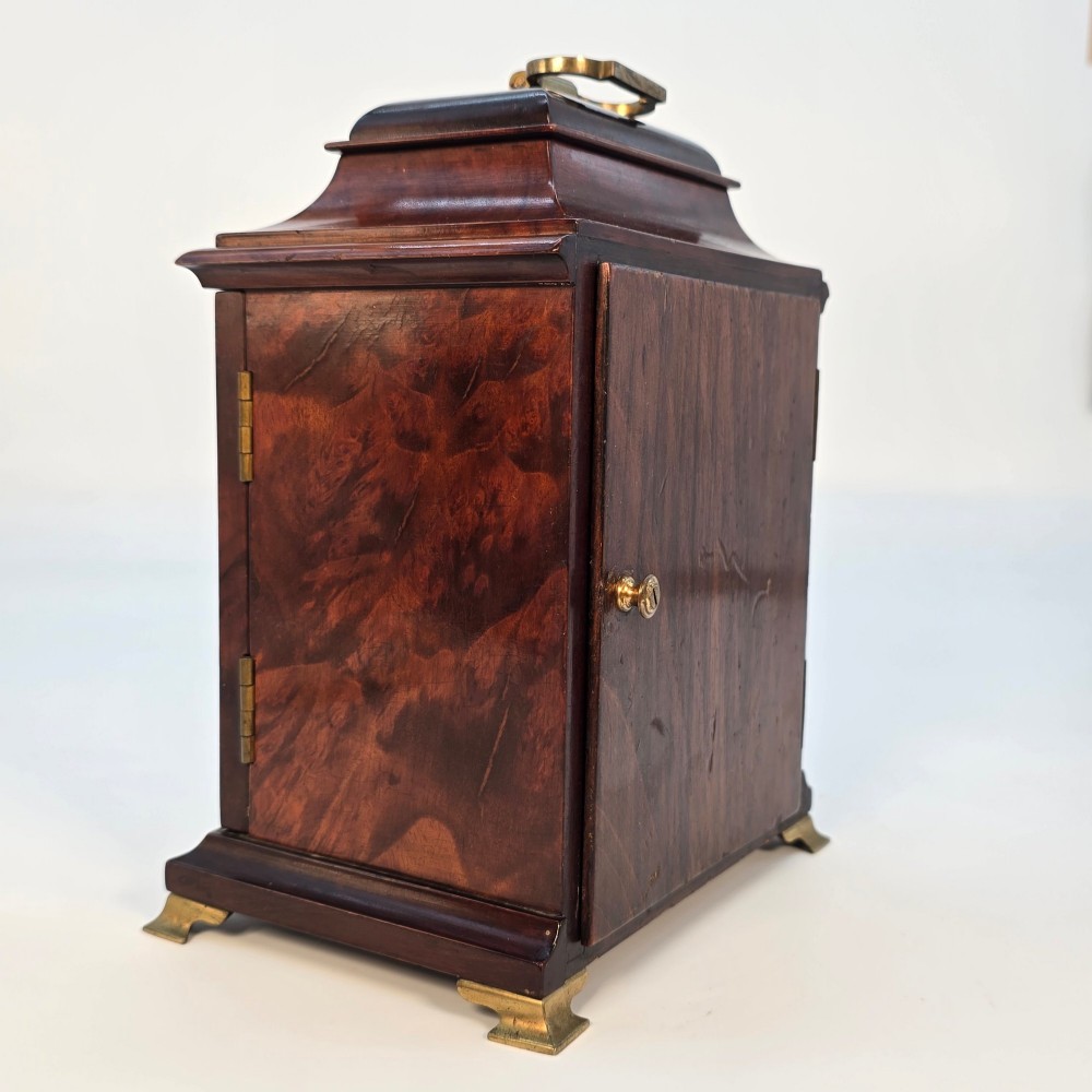 A miniature George II style wooden bracket clock featuring a caddy top with brass handle, engraved silvered dial with Roman numerals, and brass feet. View V
